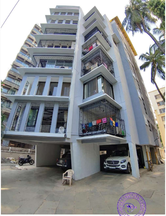 Modern multi-story residential building with balconies protected by metal grills, parked cars underneath, and palm trees nearby.