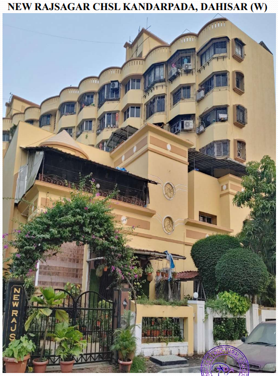 Front view of the multi-story yellow residential building New Rajsagar CHSL Kandarppada with greenery and a gated entrance.