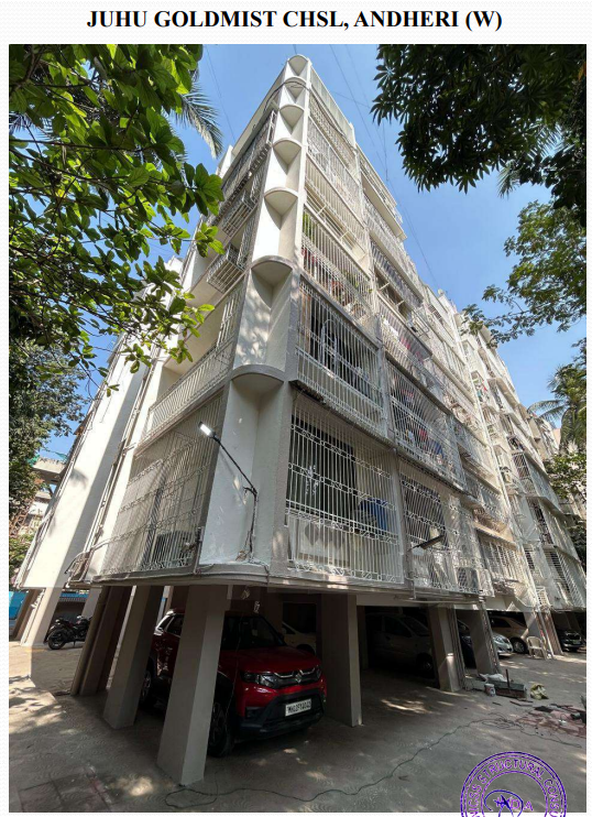 Low-angle view of a multi-story residential building with balconies enclosed by metal grills, surrounded by trees and parked cars underneath.